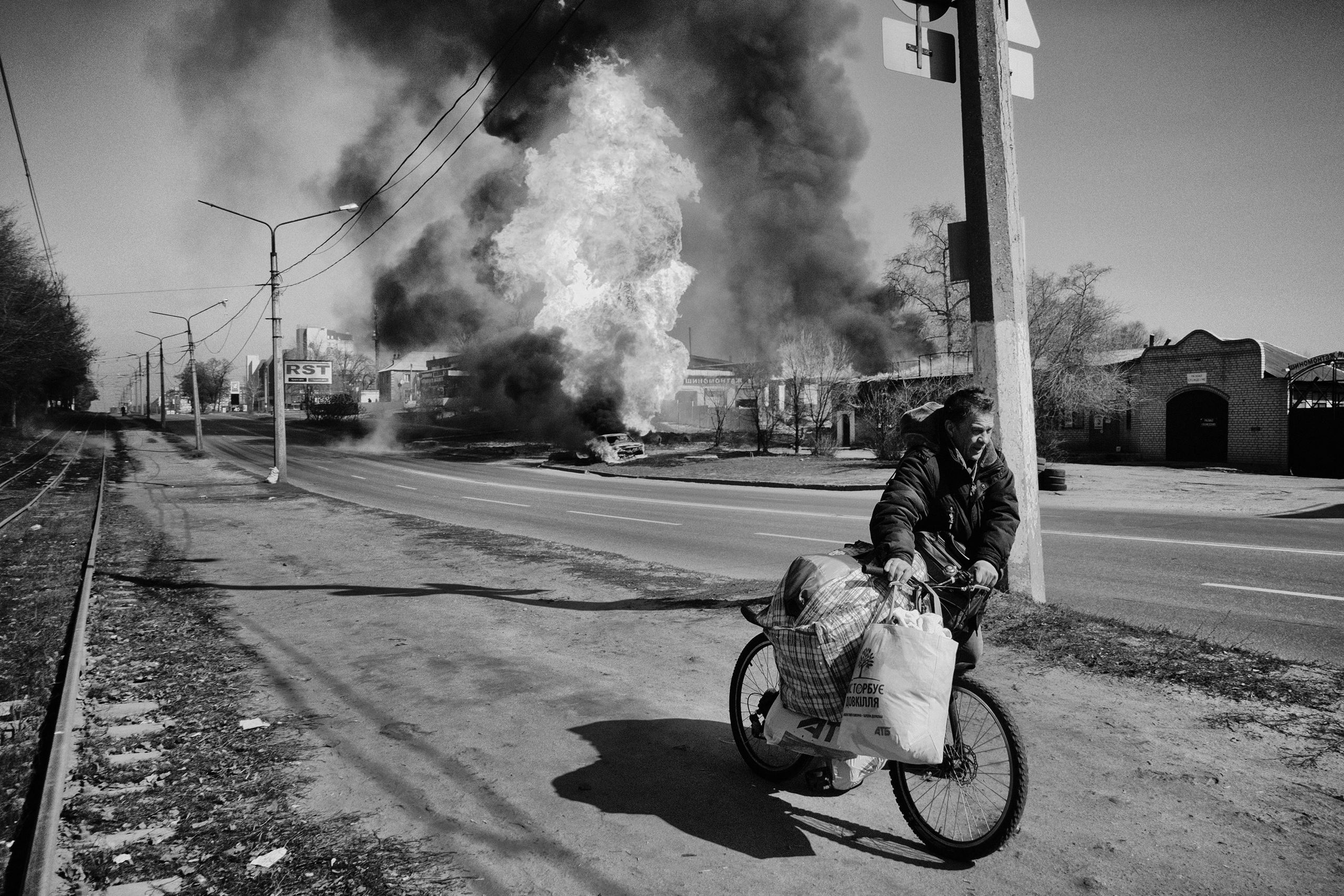 A person pushing a bike with a large fire behind them.